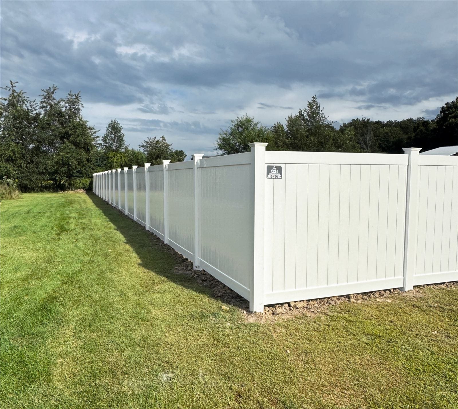 White vinyl privacy fence installed by Xcel Outdoor Living under a dramatic Illinois sky